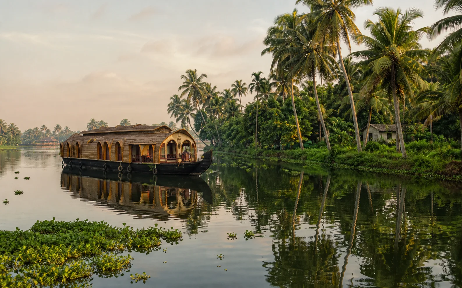 A traditional houseboat moving through the Kerala backwaters at dawn